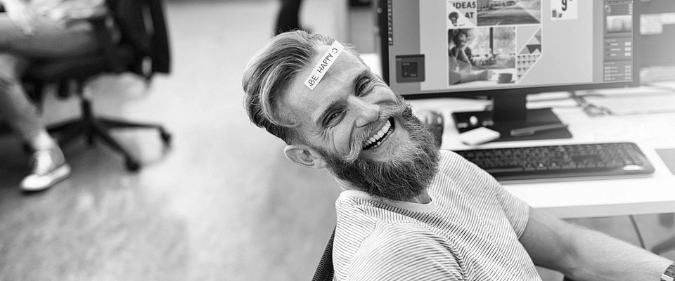 Happy office worker with beard in front of computer